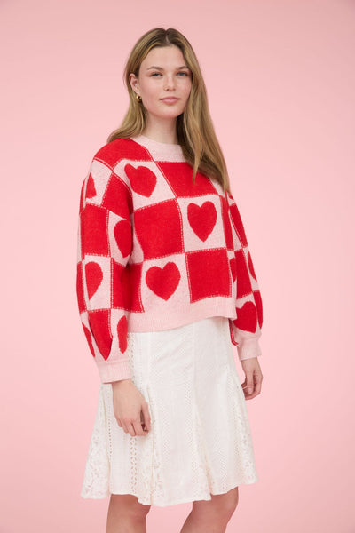 Woman wearing a red and white checkered heart-patterned sweater on a pink background
