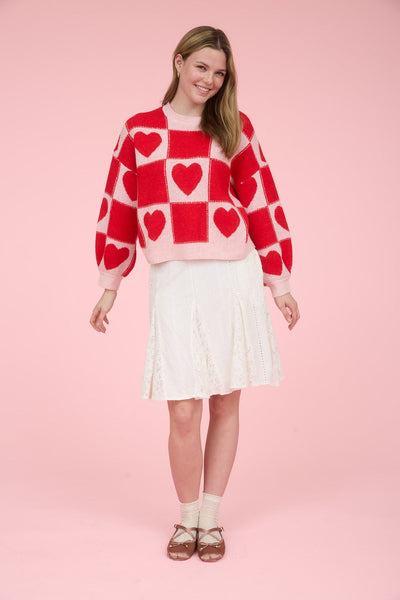 Woman wearing a red and white checkered sweater with heart patterns on a pink background