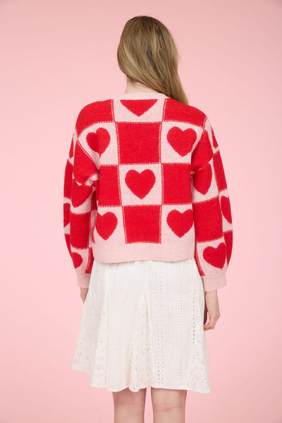 Person wearing a red and pink checkered sweater with heart patterns on a pink background