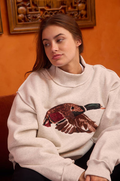 Woman wearing a light gray sweatshirt with a bird graphic in an indoor setting.