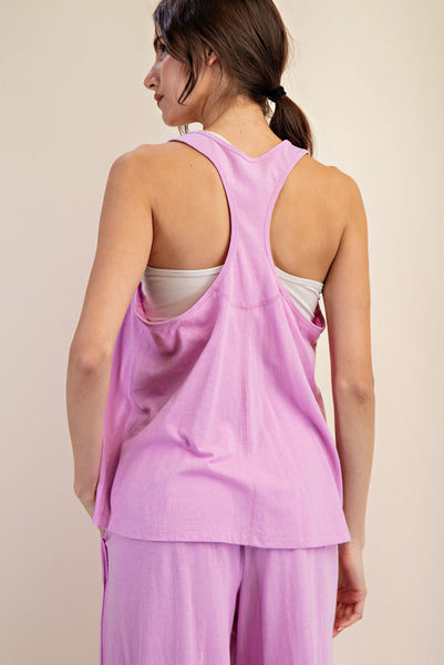 A woman shown from the back wearing a lavender-purple racerback tank top and matching lounge pants against a plain beige studio background.