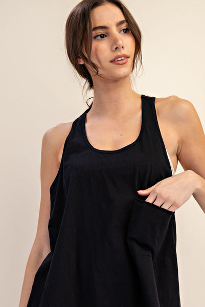 A woman wearing a black sleeveless tank top with a side pocket, photographed against a plain light beige studio background.