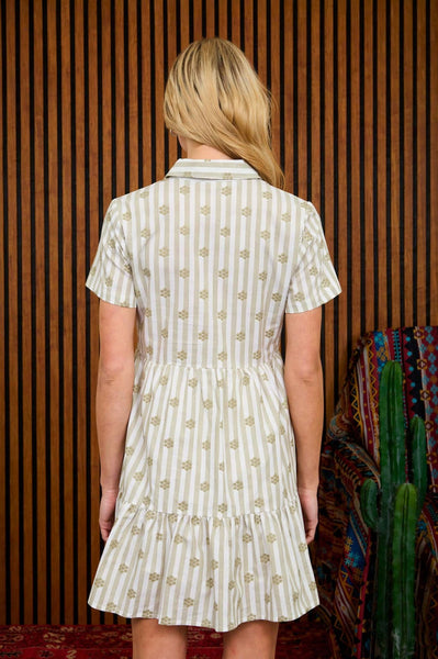 Woman wearing a patterned dress standing against a wooden paneled wall.
