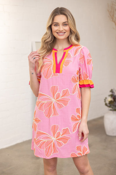Woman wearing a pink floral dress with orange accents indoors.
