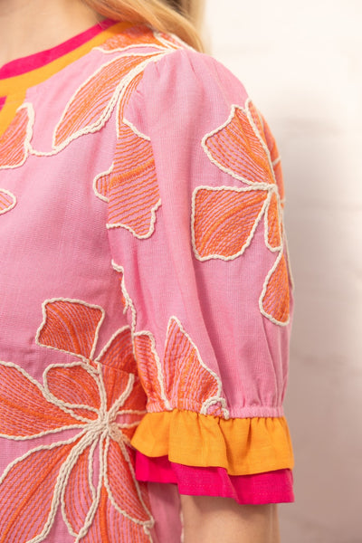 Close-up of a pink garment with orange floral embroidery on a plain background