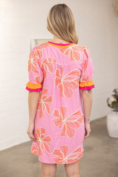 Woman wearing a pink dress with orange floral patterns indoors.