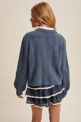Woman wearing a blue knitted cardigan and matching skirt with white trim on a beige background