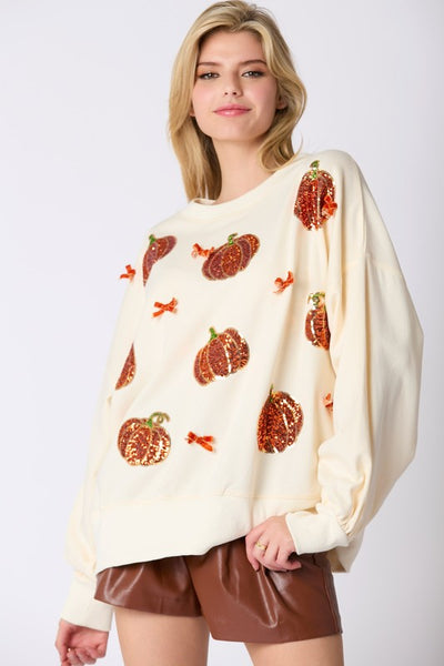 Woman wearing a cream-colored sweater with pumpkin patterns on a white background