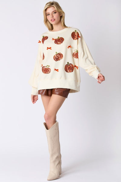 Woman wearing a cream sweater with pumpkin pattern and brown skirt on a white background