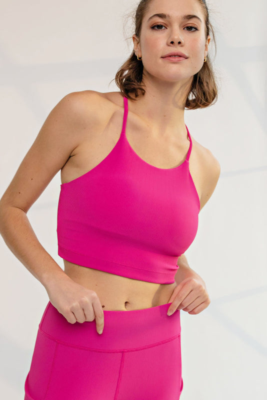 A woman modeling a bright pink athletic sports bra and matching high-waisted leggings against a light gray studio background.