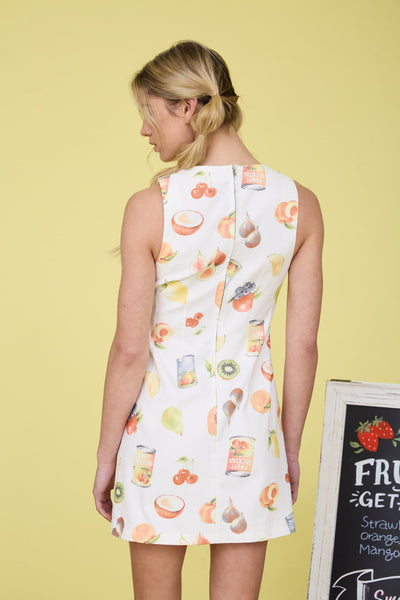 Woman wearing a sleeveless dress with fruit pattern against a yellow background