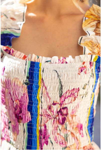 Close-up of a smocked floral top with a square neckline, featuring pink, purple, blue, yellow, and white patterns, worn by a model.