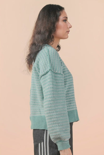 Woman wearing a teal knitted sweater against a beige background