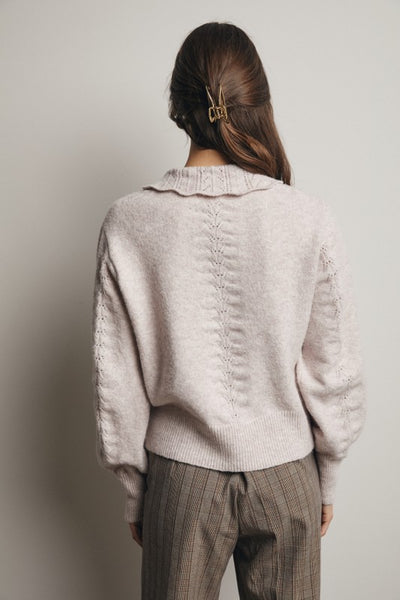 Person wearing a light gray sweater and plaid pants against a plain background