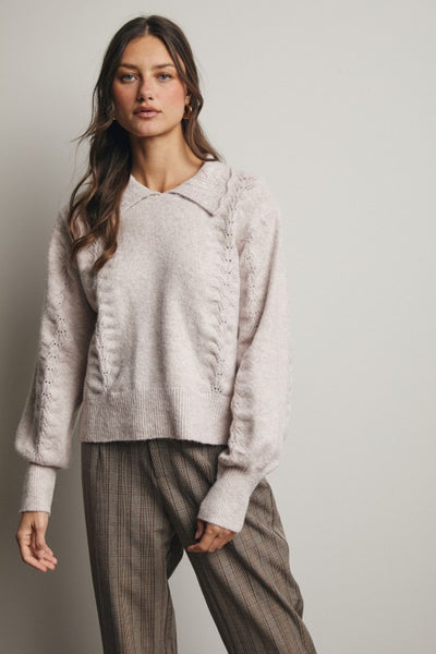Woman wearing a light gray sweater and plaid pants against a plain background