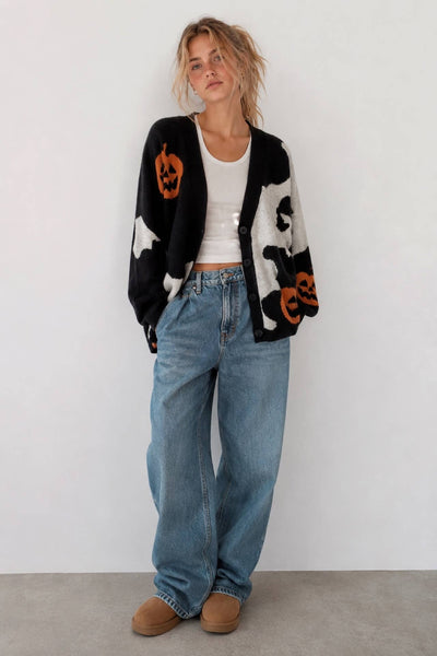 Women's oversized black and cream Halloween knit cardigan featuring orange jack-o'-lantern pumpkins, white ghosts, drop shoulders, and a button-front closure.