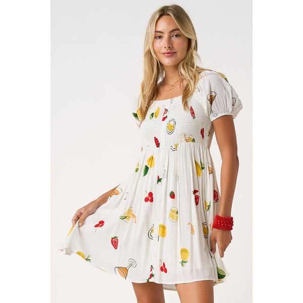Woman wearing a white dress with colorful fruit patterns on a plain background