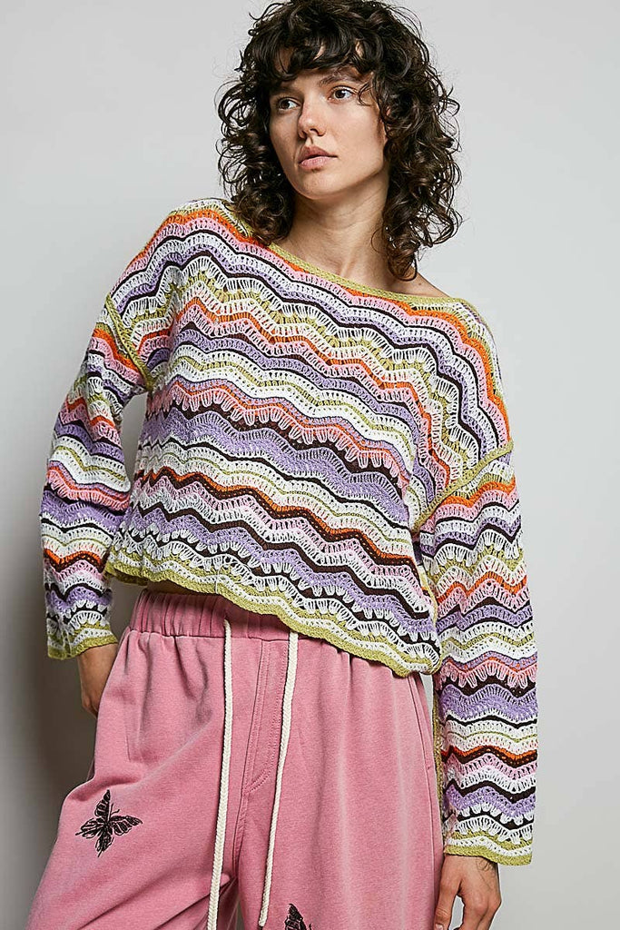 Person wearing a colorful patterned sweater and pink pants against a plain background