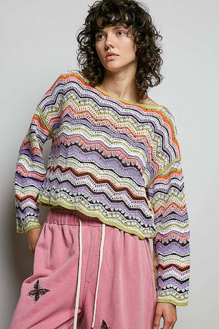 Person wearing a colorful patterned sweater and pink pants against a plain background