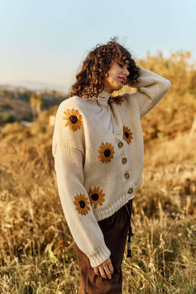 Person wearing a cream sweater with sunflower patterns in a field