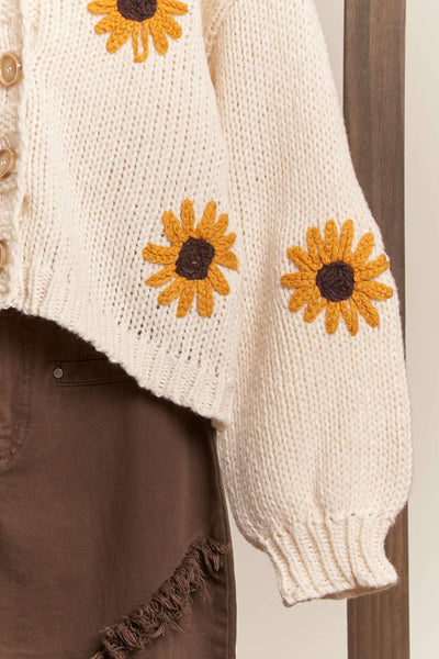 White knitted cardigan with sunflower patterns on a wooden surface
