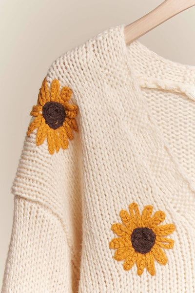 White knitted sweater with sunflower patterns on a beige background