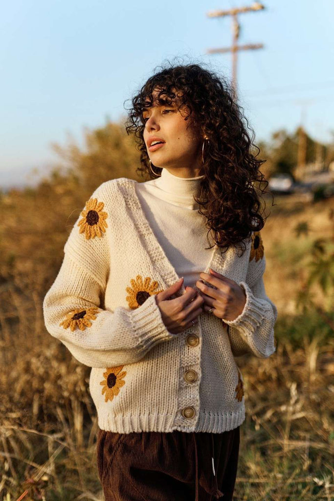 Woman wearing a white cardigan with sunflower patterns in an outdoor setting