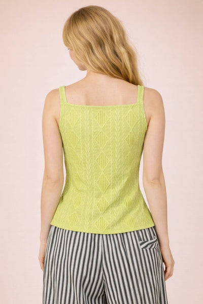 Woman wearing a light green sleeveless top with a pink background