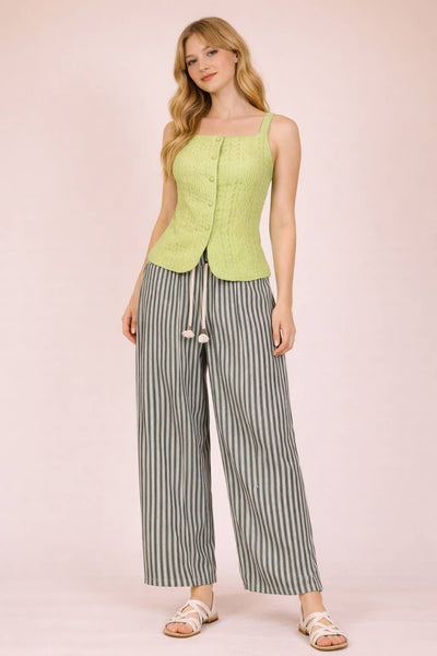 Woman wearing a light green sleeveless top and striped pants on a pink background