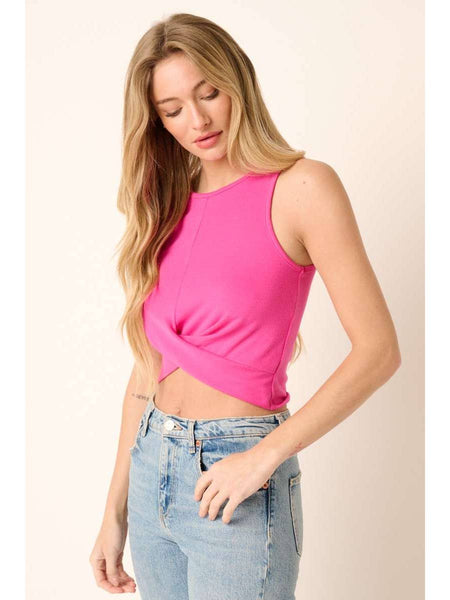 A woman wearing a bright pink sleeveless crop top with a twisted front detail and light wash blue jeans, standing against a plain beige background.