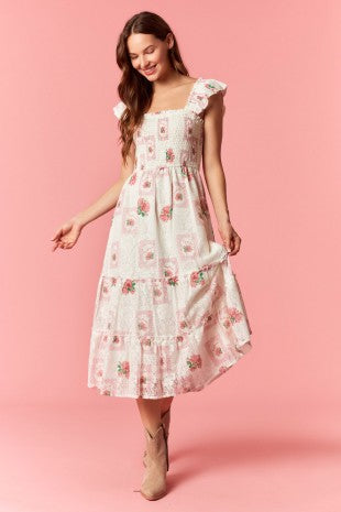 Woman wearing a vintage floral smocked midi dress with a square neckline, ruffle sleeves, and a flowy tiered skirt.