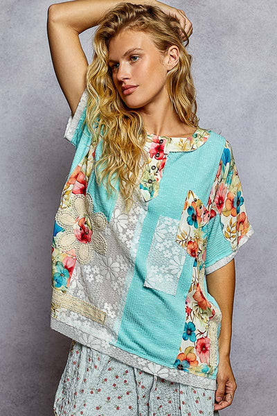Woman wearing a colorful floral and patterned top against a gray background