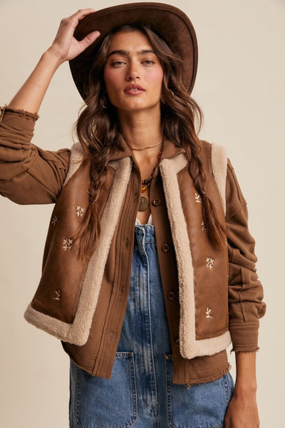 Woman wearing a brown jacket with shearling lining and a hat against a beige background