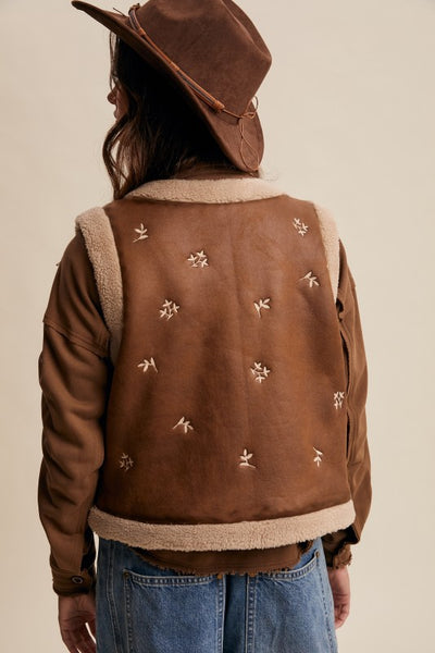 Brown leather jacket with embroidered designs on a beige background
