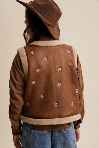 Brown leather jacket with embroidered designs on a beige background
