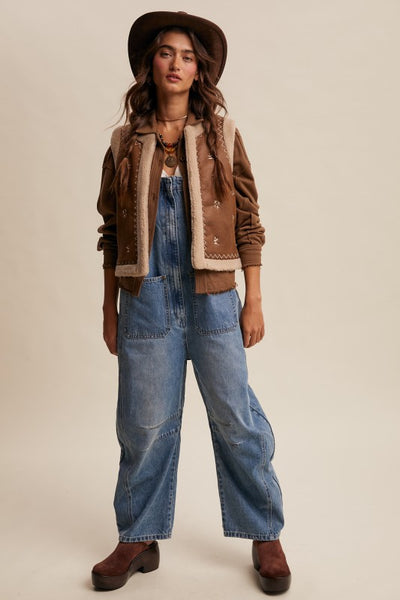 Woman wearing a brown jacket, scarf, and wide-leg jeans on a beige background