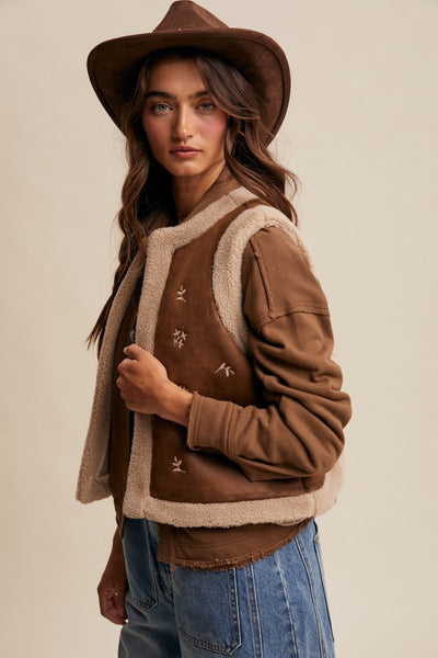 Woman wearing a brown jacket with white lining and a hat on a beige background