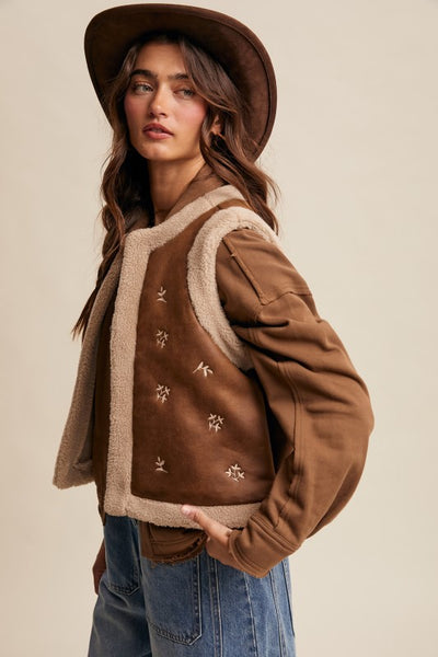Woman wearing a brown jacket with beige lining and a matching hat on a beige background