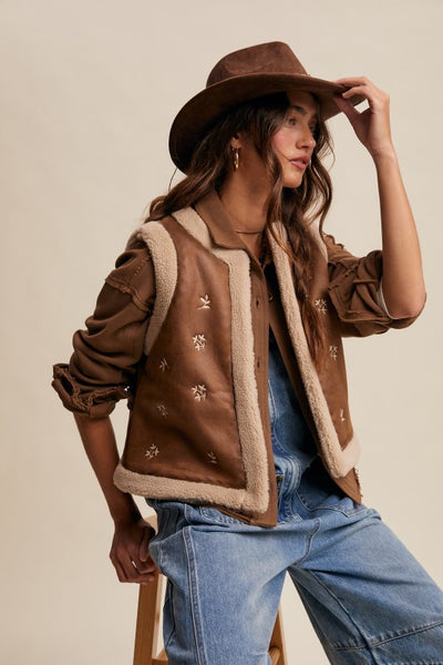 Woman wearing a brown shearling jacket and hat against a beige background